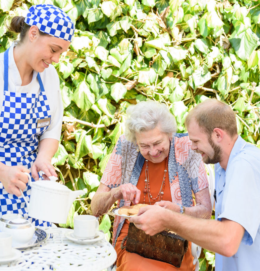 Member of kitchen staff pouring a cup of tea for elderly resident in the garden