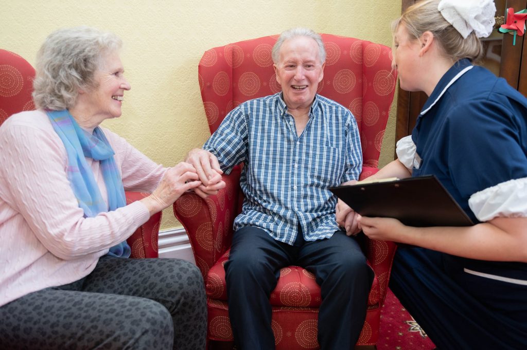 Elderly resident laughing with member of staff and elderly woman